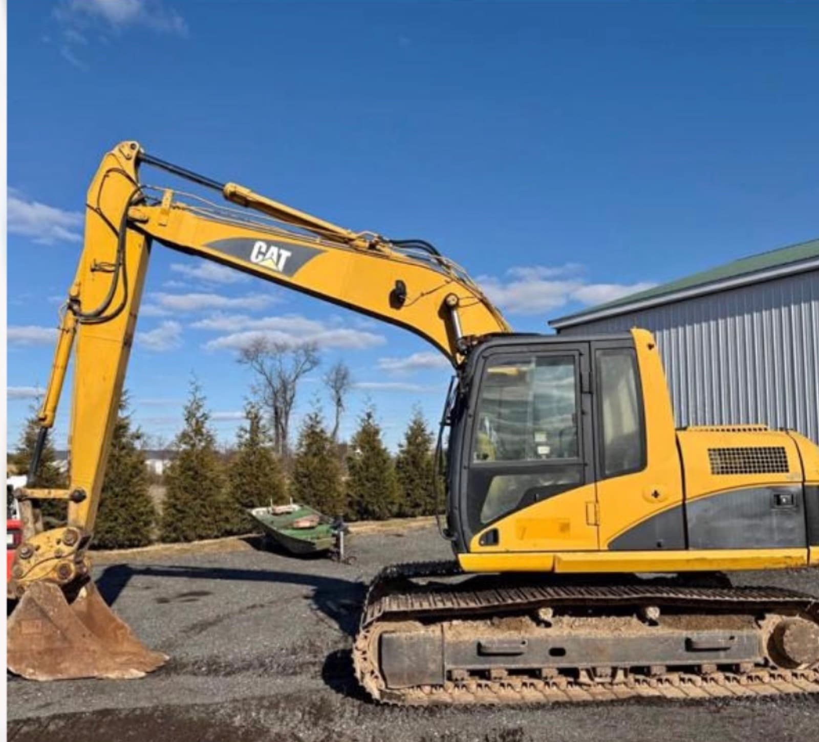 Caterpillar 315C L tracked excavator on a cleared lot lined with conifers.