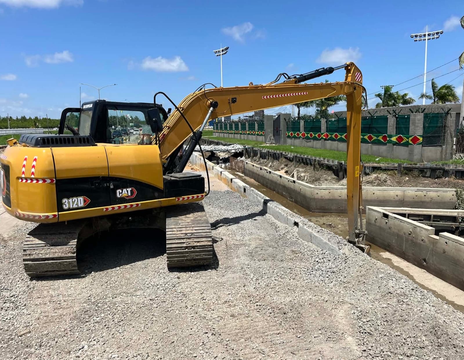 Long reach Caterpillar 312D excavator working a concrete drainage channel beside a Guyana highway.