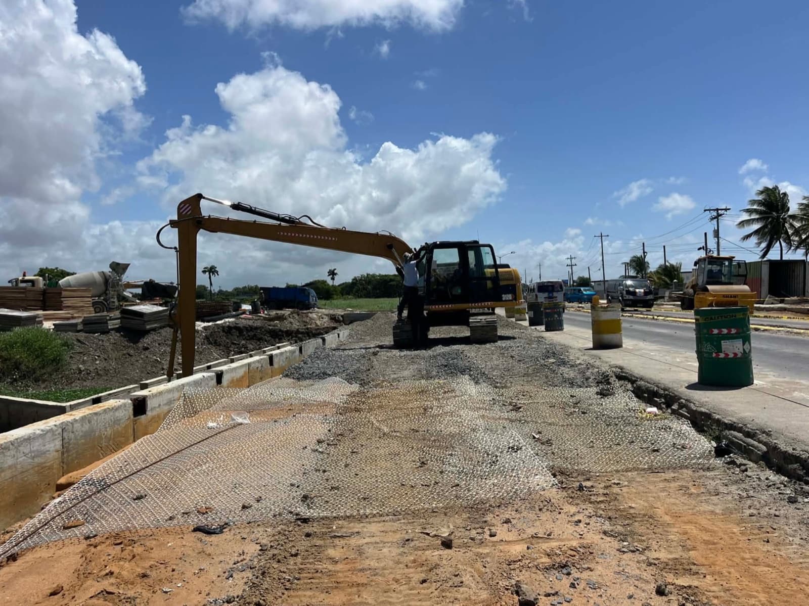Caterpillar 312D long reach excavator on a roadworks site with a smooth drum roller in the background.